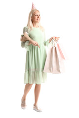 Mature woman with flowers and bags of birthday gifts on white background