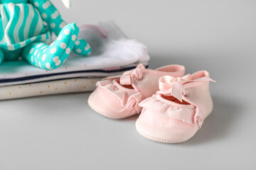 Pair of stylish baby booties and clothes on grey background
