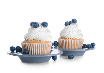 Plates of tasty cupcakes with blueberries on white background