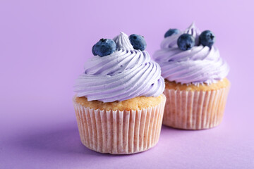 Tasty cupcakes with blueberries on lilac background