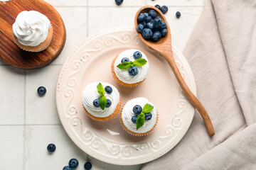 Plate of delicious cupcakes with blueberries and mint on white tile background