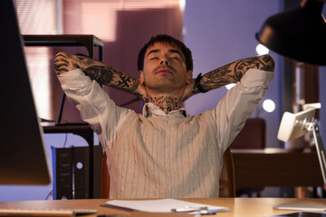 Young tattooed man resting in office at night