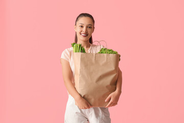 Young Asian woman with shopping bag full of fresh food on pink background