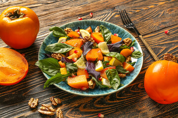Plate of delicious salad with persimmon, walnut and pomegranate seeds on wooden background