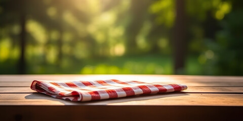 Wooden table with red and white checkered tablecloth part, forest background, picnic concept - obrazy, fototapety, plakaty