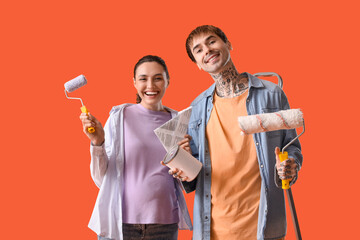 Young pregnant couple with paint can and rollers on orange background