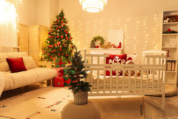Interior of bedroom with baby crib, Christmas trees and glowing lights in evening
