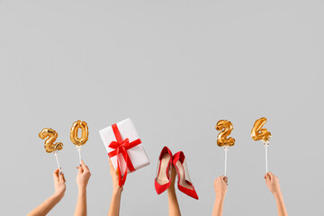 Female hands with shoes, gift and figure 2024 on white background. New year shopping concept