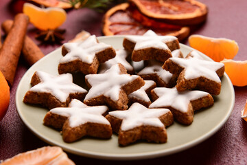 Plate with delicious stars shaped Christmas cookies with orange dried pieces and mandarin on brown background