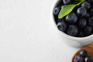 Ripe bilberries and leaf in bowl on white table, closeup. Space for text