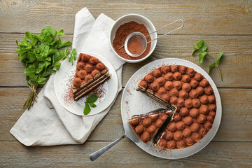 Delicious tiramisu cake, cocoa powder, server and mint leaves on wooden table, flat lay