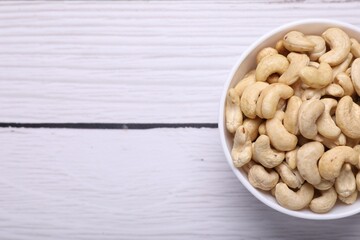 Tasty cashew nuts in bowl on white wooden table, top view. Space for text
