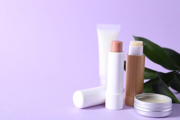 Different lip balms and leaves on lilac background, closeup. Space for text