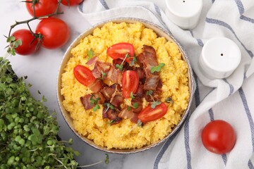Tasty cornmeal with tomatoes, bacon and microgreens in bowl served on white table, flat lay
