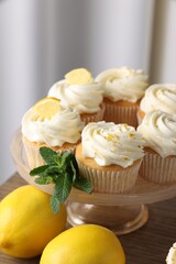 Delicious lemon cupcakes with white cream, mint and lemons on table, closeup