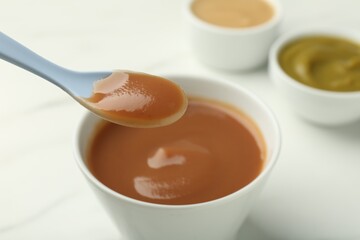 Eating healthy baby food with spoon at white table, closeup