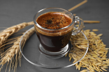 Cup of barley coffee, grains and spikes on gray table, closeup
