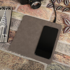 Charging the smartphone with leather wireless charger on desk. Gray color leather charger pads. Wireless mousepad, Charger pad. Closeup, top view, no people. Concept shoot.