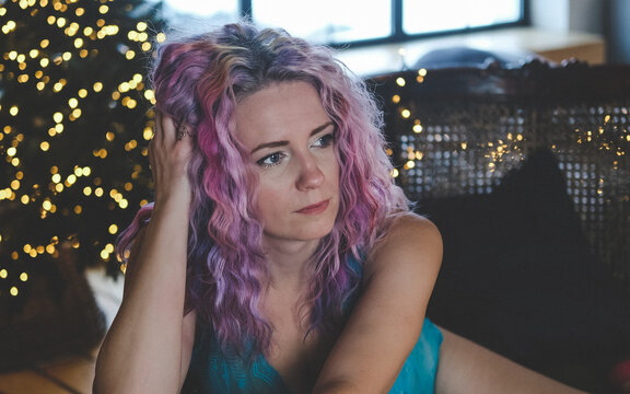 Gorgeous woman with bright multi-colored hair posing in blue lingerie near a Christmas tree
