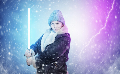 A young woman in winter clothes holds a light sword  in her hands, snow is swirling around, on a...