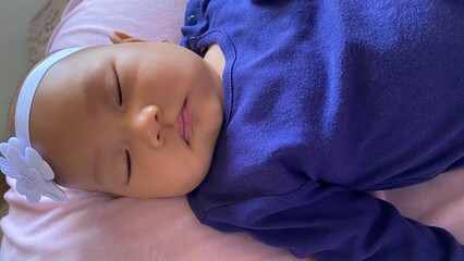 Cute Asian baby with natural expression, wearing navy blue clothes and white headband. was lying on a pink mattress