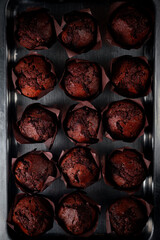 Multi-chocolate muffin with chocolate pieces on a steel baking tray, top view