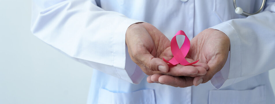 Breast cancer campaign Cropped image of woman's hand in doctor's uniform with pink ribbon in hospital showing fight To save lives and illnesses from cancer World cancer day concept, health insurance.