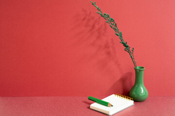 Notepad and colored pencil with vase of plant on red desk. red wall background, workspace