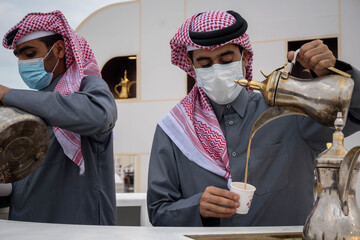 A young Qatari Arab in traditional dress pours Arabic coffee from the pot into the cup at Al Darab Saai at Umm Salal Mohamad in Doha, Qatar. During celebrate Qatar national day.