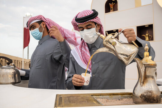 A young Qatari Arab in traditional dress pours Arabic coffee from the pot into the cup at Al Darab Saai at Umm Salal Mohamad in Doha, Qatar. During celebrate Qatar national day.