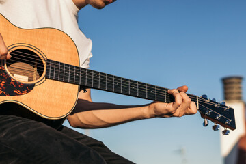 young man sitting playing acoustic guitar on a rooftop. close-up