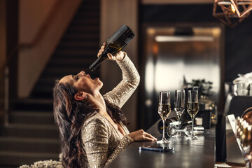 A tipsy woman drinks the last drops of champagne after New Years in the late morning at a bar