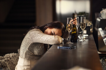 A drunk woman in a bar has fallen asleep on the bar counter, next to her is an empty champagne bottle and half-finished glasses - obrazy, fototapety, plakaty