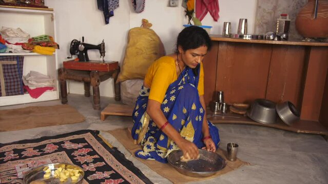 A middle-aged lower-class family lady is kneading the wheat dough for Chapatis / Rotis  small house  single room  migrant worker  dark skin. A rural Indian woman kneading the dough while adding wat...