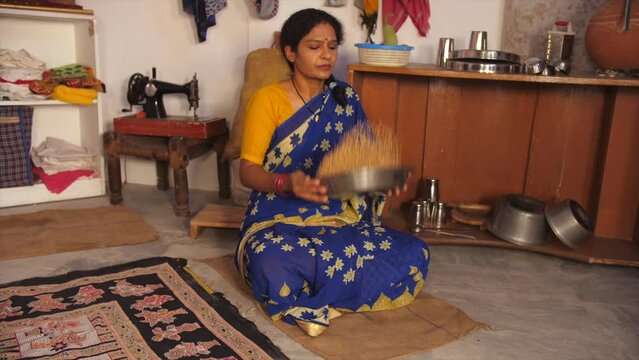 A middle-aged lady in her late forties - cleaning wheat  household daily chores  Indian home  lower middle-class single lady. A rural housewife from a village is picking dirt particles from the ric...