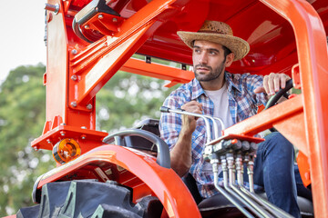 A male farmer in a plaid shirt and hat tests a tractor before buying at a trade show..