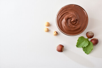 Cocoa cream with hazelnuts around in glass bowl isolated  white