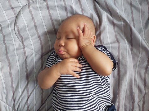 A cute baby with a natural expression wearing a striped shirt, lying on the bed