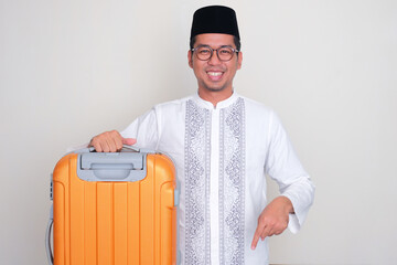 Moslem Asian man carrying suitcase with happy expression pointing below