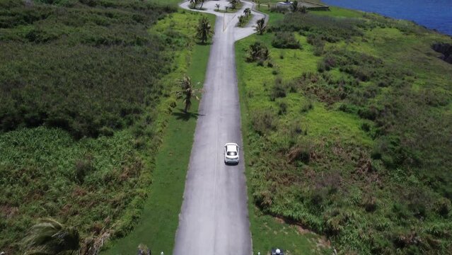 Tilt up drone shot of a white car driving along Banzai Cliff at Tinian island