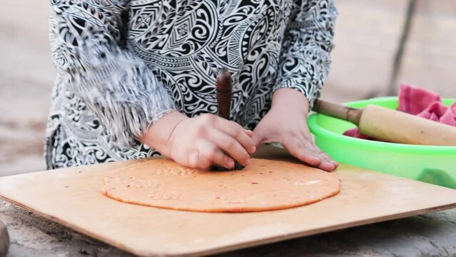 Drawing a pattern on an Uzbek flatbread using a special device called chekich. Close-up of woman's hands baking flatbreads in tandoor oven