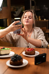Young Caucasian woman taking photos of food and desserts in a cafe using a mobile phone to create content