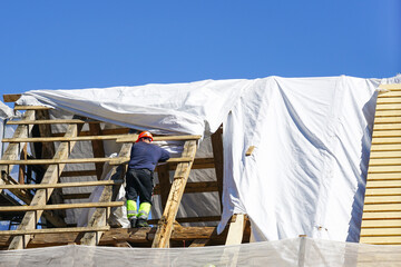 A worker replaces the damaged roof structures of an old wooden house, white safety net, blue sky