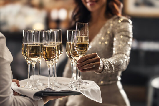 A bartender holds a plate with pink champagne and a woman in a cocktail dress takes one of the glasses at an event, party or wedding