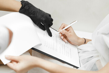 female client signs consent form while sitting during medical consultation with cosmetologist....