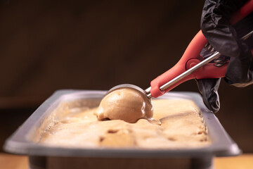 Close-up stainless steel ice cream scoop is scooping chocolate ice cream.