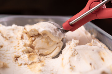 Close-up of a scoop scooping vanilla caramel ice cream from a container