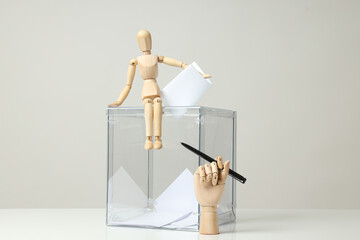 Transparent box, voting papers, wooden man and hand with pen on gray background