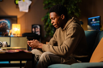 Talanted African American dark skinned writer using phone to research topics and take notes while typing up articles or stories on his laptop.