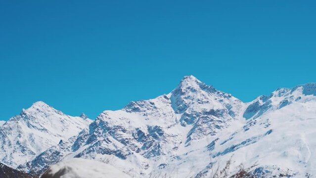 4K shot of snowy mountain peaks against the clear blue sky during the winter season at Keylong in Lahaul Valley, Himachal Pradesh, India. Snow covered Himalayan mountain peaks during the winter. 